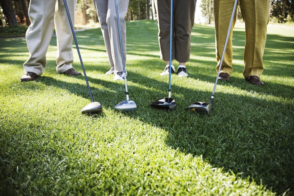 Closeup of the feet of four golfers and the head of their driver clubs.